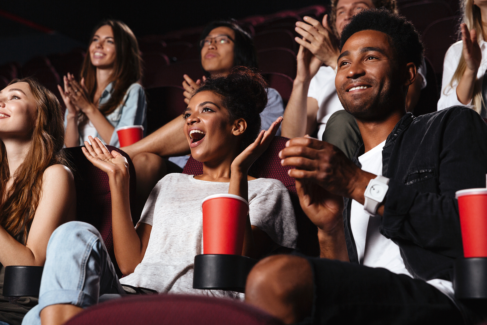 REVIVE.ORG - Multiethnic happy audience clapping hands while sitting at the cinema and watching movie